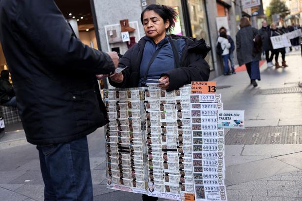 Una persona compra billetes de lotería de Navidad a una vendedora ambulante frente al popular establecimiento de lotería 'Dona Manolita' el 18 de diciembre de 2023 en el centro de Madrid (Foto: Thomas Coex / AFP)