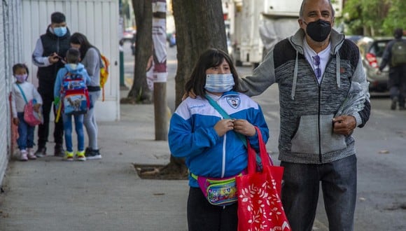 Una niña es acompañada por un familiar mientras camina a su escuela durante la reanudación de las clases presenciales en la Ciudad de México. (CLAUDIO CRUZ / AFP)