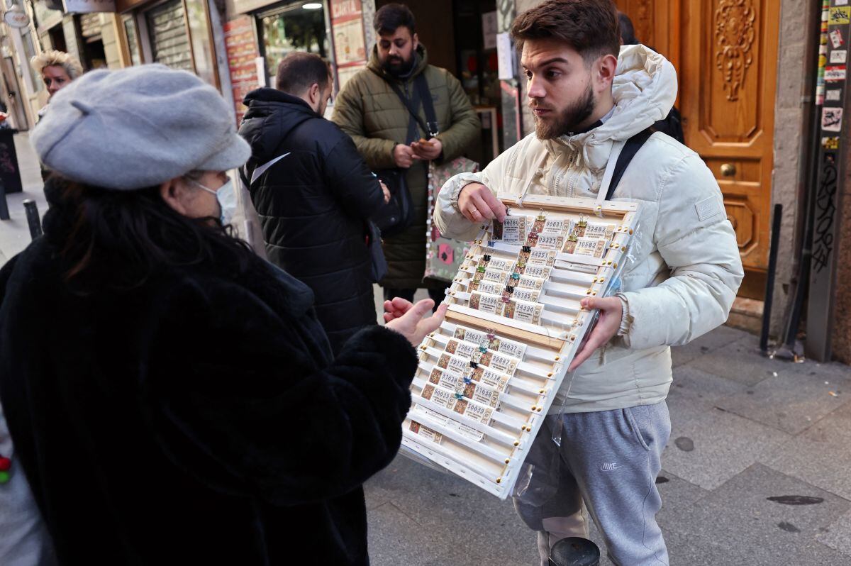 Una persona compra billetes de lotería de Navidad a un vendedor ambulante frente al popular establecimiento de lotería 'Dona Manolita' el 18 de diciembre de 2023 en el centro de Madrid (Foto: Thomas Coex / AFP)