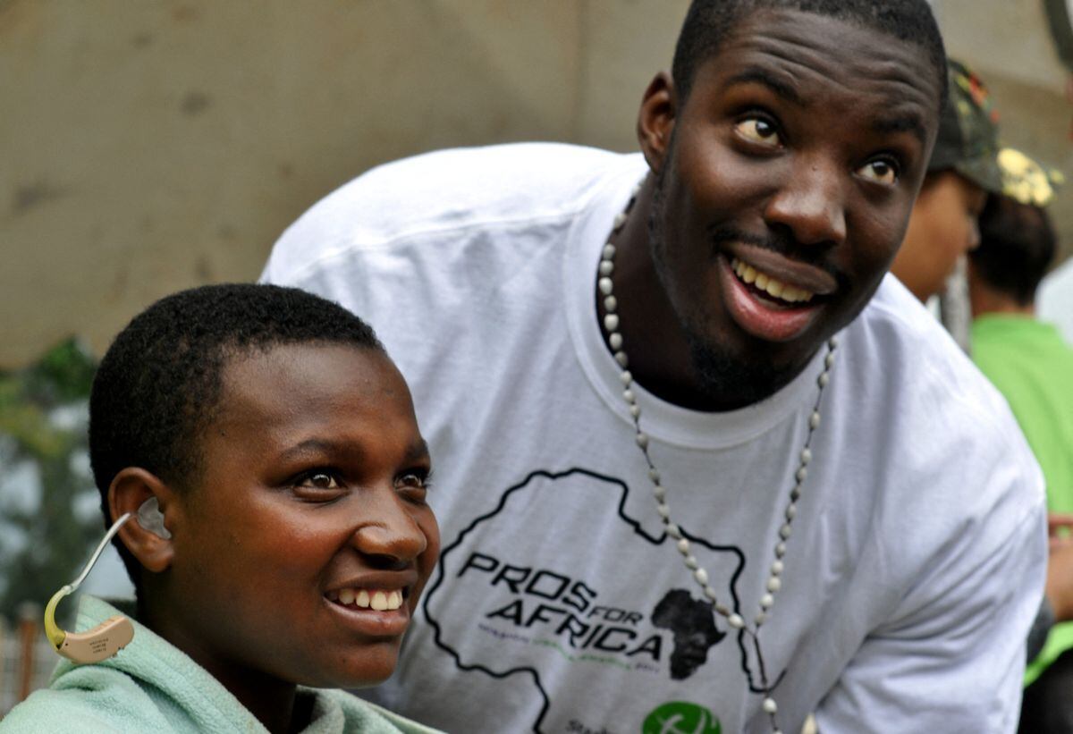 Esta fotografía tomada el 21 de marzo de 2011 muestra al Vontae Davis, entonces defensa de los Miami Dolphins, levantar la vista para consultar con su intérprete mientras le coloca un audífono a un niño en Musanze, Ruanda (Foto: Steve Terill / AFP)