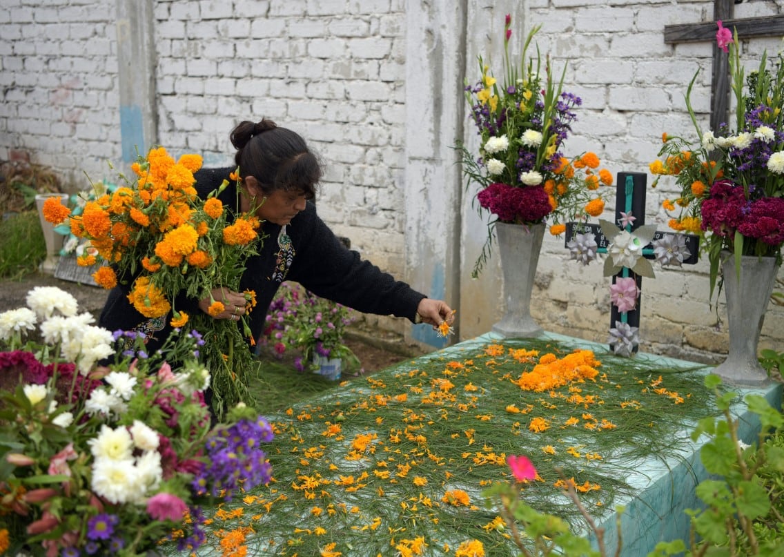 Una señora colocando flores de cempasúchil en la tumba de su familiar (Foto: AFP)